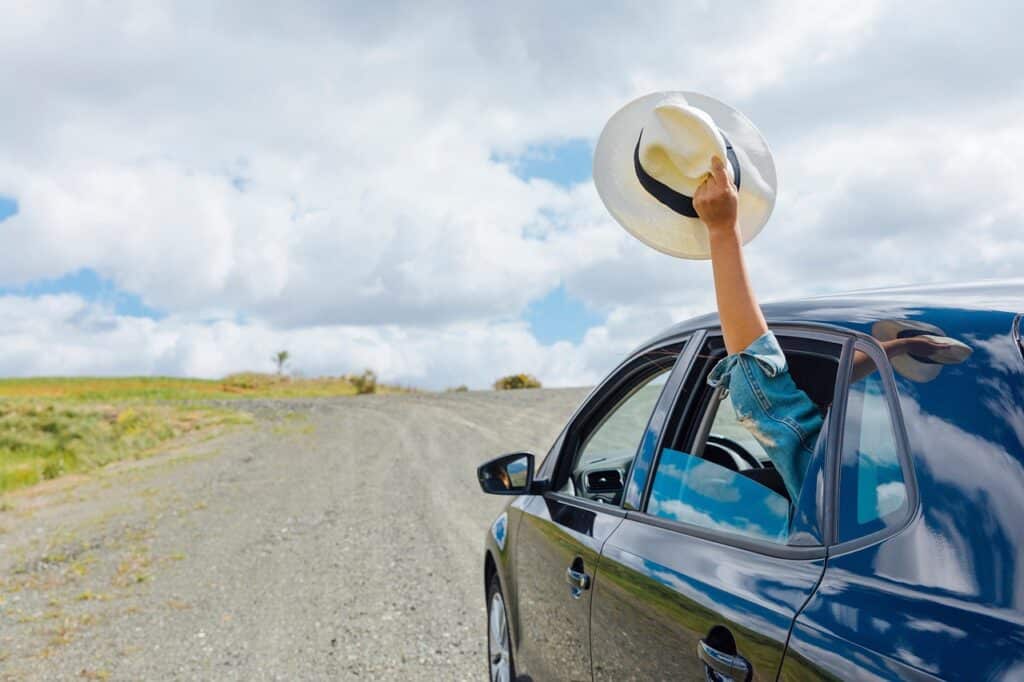 une dame agite son chapeau par la fenêtre de sa voiture